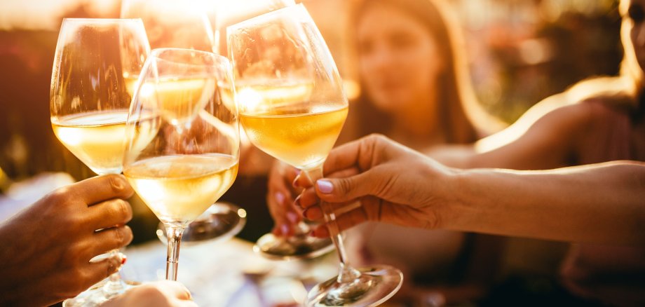 Fünf in Händen gehaltene Weingläser mit Weißwein prosten sich zu.