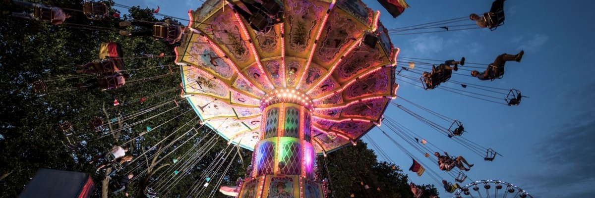 Eine Aufnahme des Kettenkarussels auf dem Fischefest um die Dämmerung herum von unten fotografiert Es wirkt als würden die Fahrgeäste über einen hinweg kreisen Das Fahrgeschäft ist hell erleuchtet 