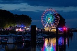 Der nächtliche Blick auf die Hafenspitze zum Fischerfest alles ist bunt in lila pink gelb beleuchtet und das Wasser im Hafenbecken reflektiert die Lichter