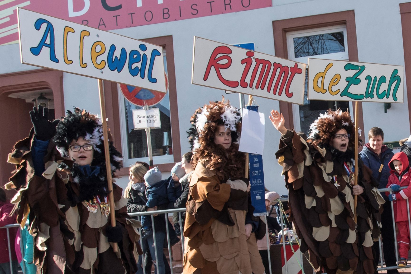 Drei Kinder in Eulenkostümen mit Schildern Alleweil kimmt der Zuch.