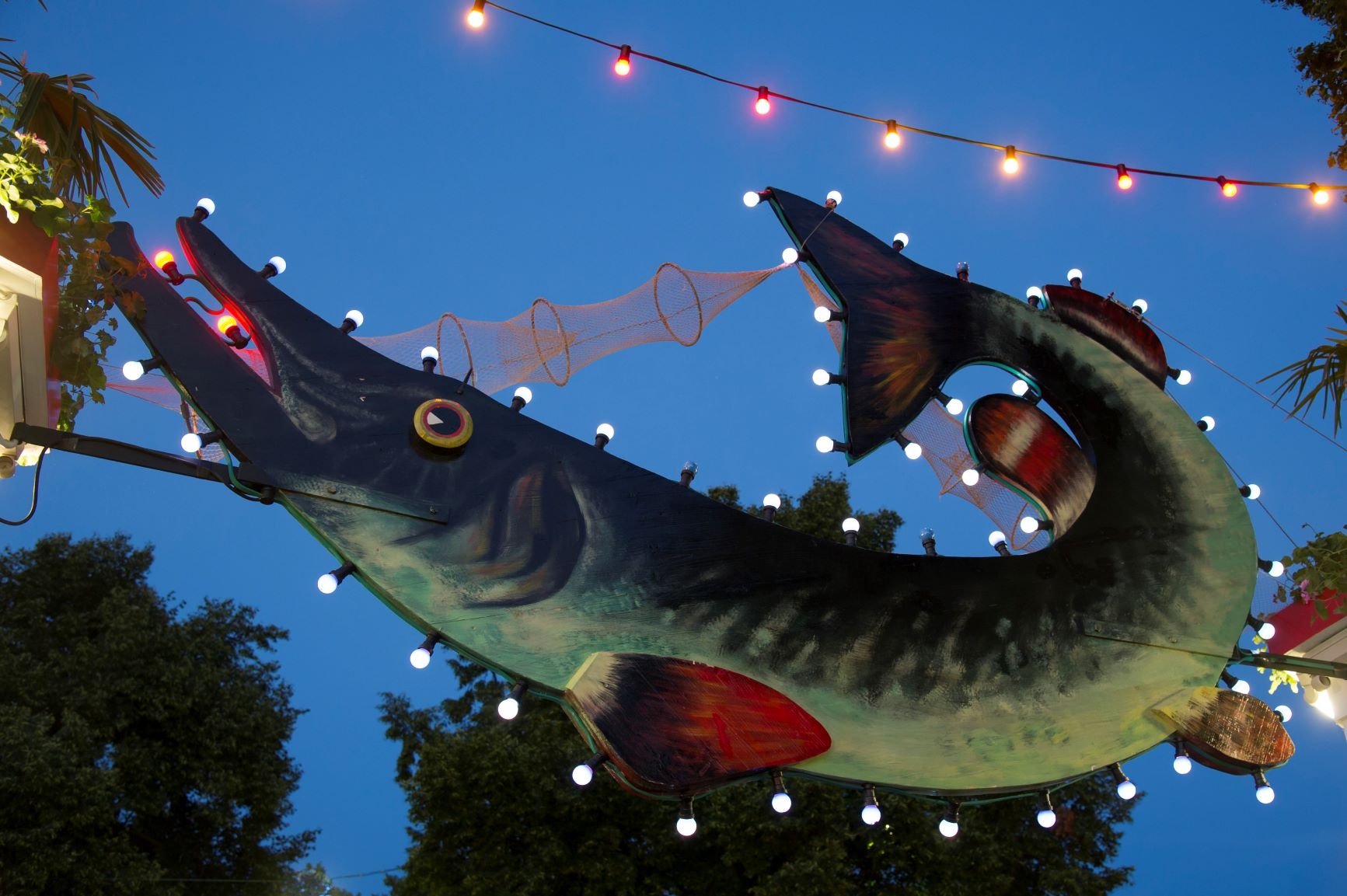 Der große grüne Hecht über dem Haupteingang des Festgeländes des Fischfests wie er in den Abenstunden bei Dämmerung beleuchtet ist.