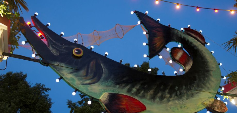 Der große grüne Hecht über dem Haupteingang des Festgeländes des Fischfests wie er in den Abenstunden bei Dämmerung beleuchtet ist.