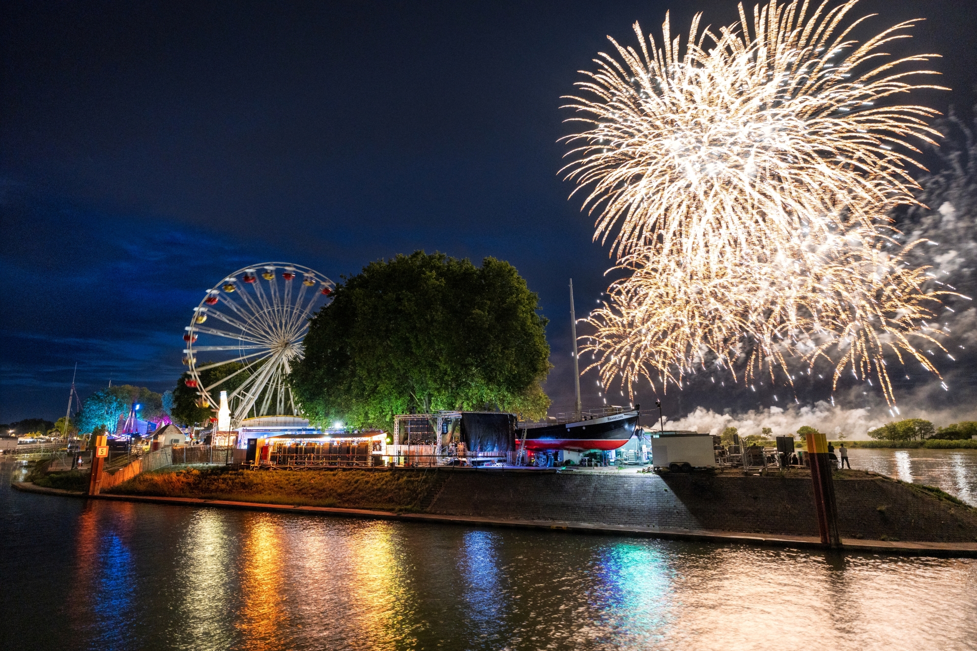 Feuerwerk über der Hafenspitze beim Fischerfest. Rechts ein weiß leuchtendes Feuerwerk über dem Aalschocker Hannelore. Links das Riesenrad.
