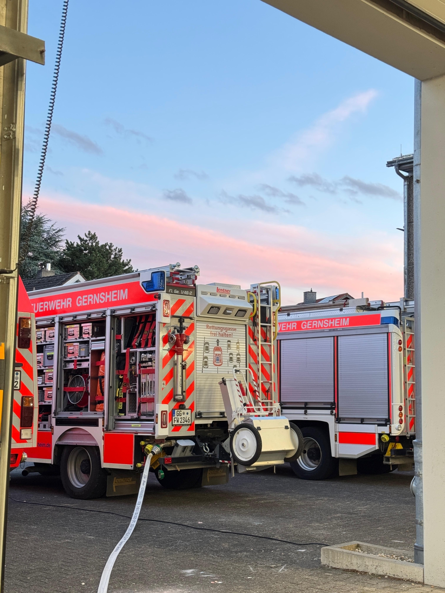 Zwei Feuerwehrfahrzeuge von der Seite. An eines ist ein Schlauch angeschlossen.