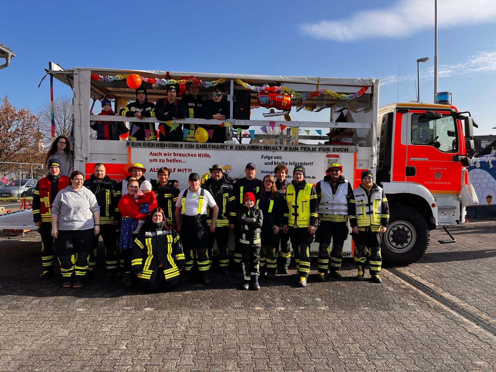 Feuerwehrleute beim Fastnachtsumzug vor einem Feuerwehrfahrzeug.