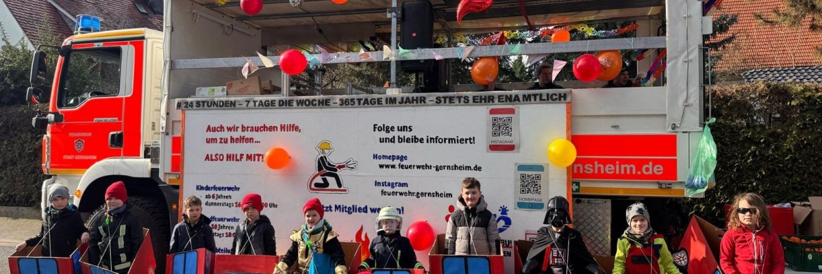 Kinder der Jugendfeuerwehr beim Fastnachtsumzug vor einem Feuerwehrfahrzeug.