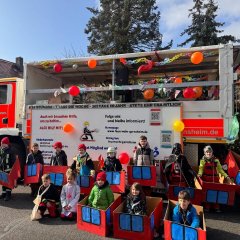 Kinder der Jugendfeuerwehr beim Fastnachtsumzug vor einem Feuerwehrfahrzeug.
