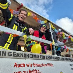 Feuerwehrleute auf einem dekorierten Umzugswagen bei der Straßenfastnacht.