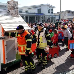 Kinder der Kinderfeuerwehr beim Umzug der Straßenfastnacht. Links im Bild auf einem Rollwagen ein Rauchaus mit dem Wappen der Schöfferstadt Gernsheim.