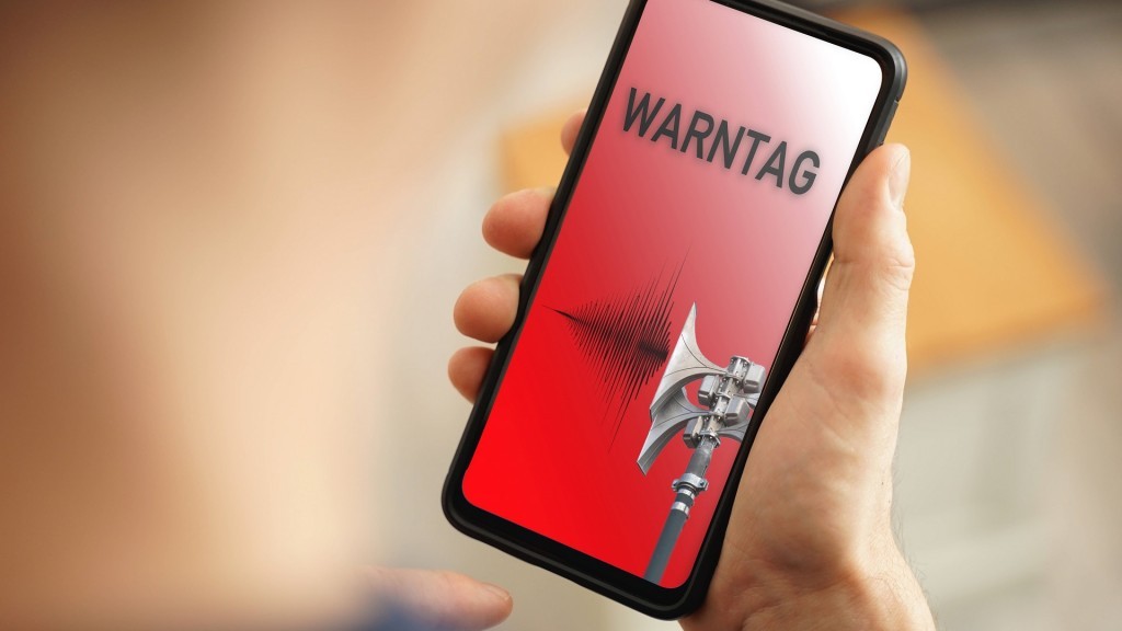 Eine Hand hält ein Smartphone. Auf dem roten Display steht das Wort Warntag. Der Hintergrund ist verschwommen.