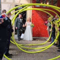 Ein Brautpaar durchschreitet ein Spalier aus Feuerwehrschläuchen. Diese werden von Feuerwehrleuten gehalten.