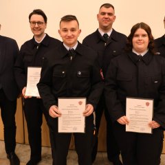 Fünf Feuerwehrangehörige in Uniform stehen in einer Reihe und halten bei der Jahreshauptversammlung 2025 der Feuerwehr Gernsheim Auszeichnungen und Urkunden. An der linken Seite steht der Bürgermeister.