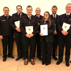 Acht Feuerwehrangehörige in Uniform stehen in einer Reihe und halten bei der Jahreshauptversammlung 2025 der Feuerwehr Gernsheim Auszeichnungen und Urkunden. An der linken Seite steht der Bürgermeister.