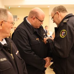 Ein Feuerwehrangehöriger wird bei der Jahreshauptversammlung 2025 mit einer Ehrennadel von einem Kameraden in Uniform dekoriert.