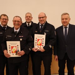 VierFeuerwehrangehörige in Uniform stehen in einer Reihe und halten bei der Jahreshauptversammlung 2025 der Feuerwehr Gernsheim Auszeichnungen und Urkunden. An der rechten Seite steht der Bürgermeister.