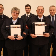 Vier Feuerwehrangehörige in Uniform stehen in einer Reihe und halten bei der Jahreshauptversammlung 2025 der Feuerwehr Gernsheim Auszeichnungen und Urkunden. An der rechten Seite steht der Bürgermeister.