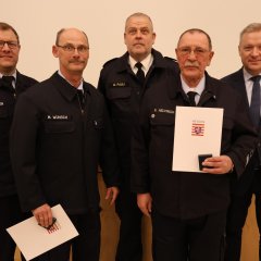 Vier Feuerwehrangehörige in Uniform stehen in einer Reihe und halten bei der Jahreshauptversammlung 2025 der Feuerwehr Gernsheim Auszeichnungen und Urkunden. An der rechten Seite steht der Bürgermeister.