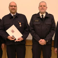 Drei Feuerwehrangehörige in Uniform stehen in einer Reihe und halten bei der Jahreshauptversammlung 2025 der Feuerwehr Gernsheim Auszeichnungen und Urkunden. An der rechten Seite steht der Bürgermeister.