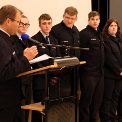 Bei der Jahreshauptversammlung der Feuerwehr Gernsheim 2025 liest ein Feuerwehrmann am Rednerpult vor, während 11 Feuerwehrleute neben ihm stehen und zuhören.