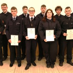 12 Feuerwehrangehörige in Uniform stehen in einer Reihe und halten bei der Jahreshauptversammlung 2025 der Feuerwehr Gernsheim Auszeichnungen und Urkunden. An der rechten Seite steht der Bürgermeister.