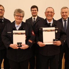 Vier Feuerwehrangehörige in Uniform stehen in einer Reihe und halten bei der Jahreshauptversammlung 2025 der Feuerwehr Gernsheim Auszeichnungen und Urkunden. An der rechten Seite steht der Bürgermeister.