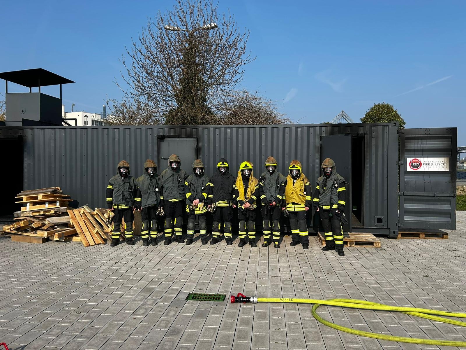 9 Atemschutzgeräteträger in ihrer PSA vor dem Realbrandcontainer.