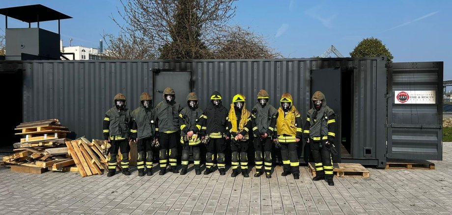 9 Atemschutzgeräteträger in ihrer PSA vor dem Realbrandcontainer.