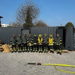 9 Atemschutzgeräteträger in ihrer PSA vor dem Realbrandcontainer.