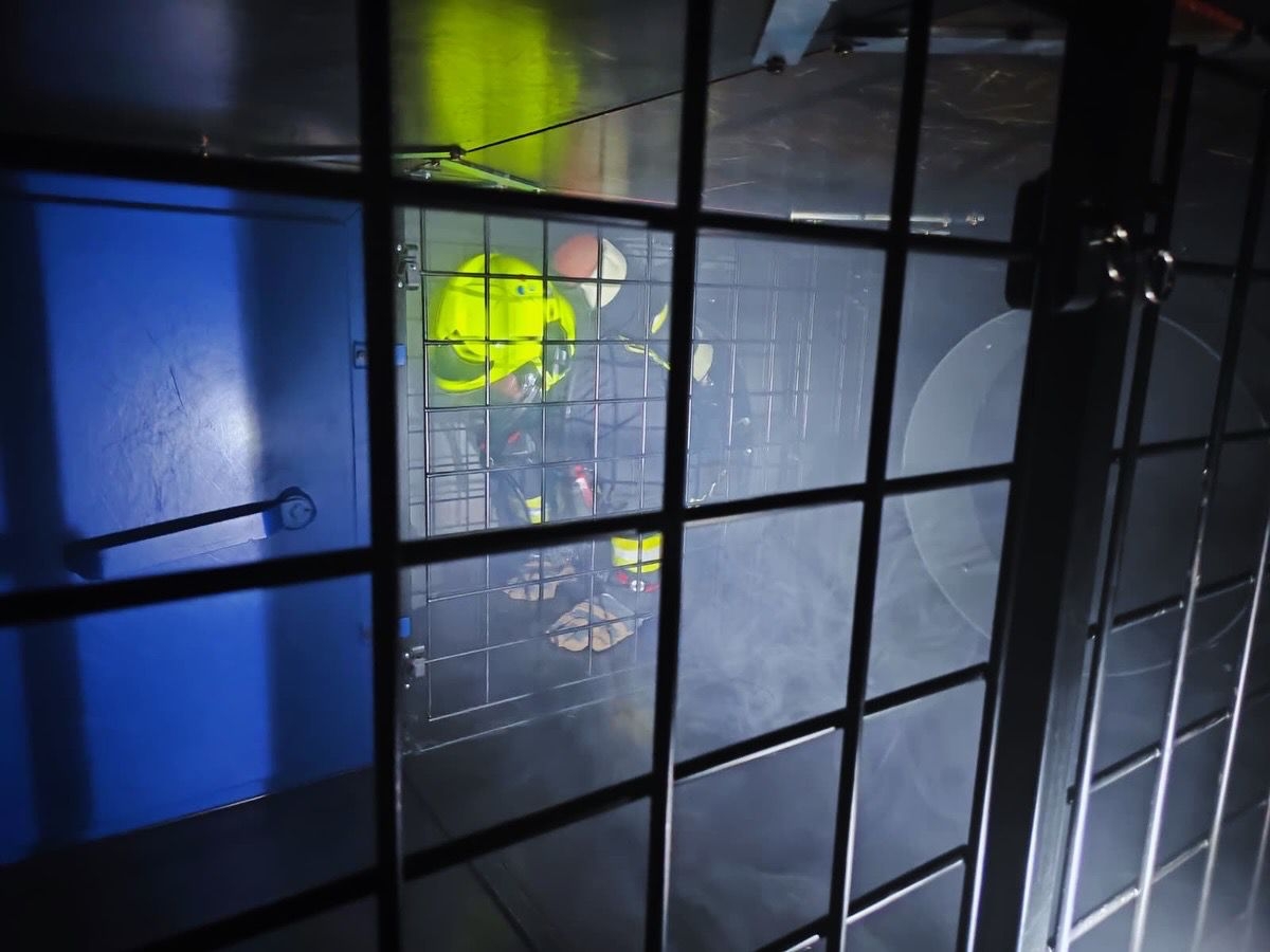 Ein Feuerwehrangehöriger in Schutzkleidung mit gelbem Helm kriecht durch einen engen, gitterartigen Parcours bei einer Atemschutz‑Streckendurchgangs‑Übung.