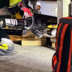 Ein Feuerwehrmann in Einsatzkleidung kniet an einem Anhänger während einer technischen Rettungsübung und setzt einen Spreitzer an.