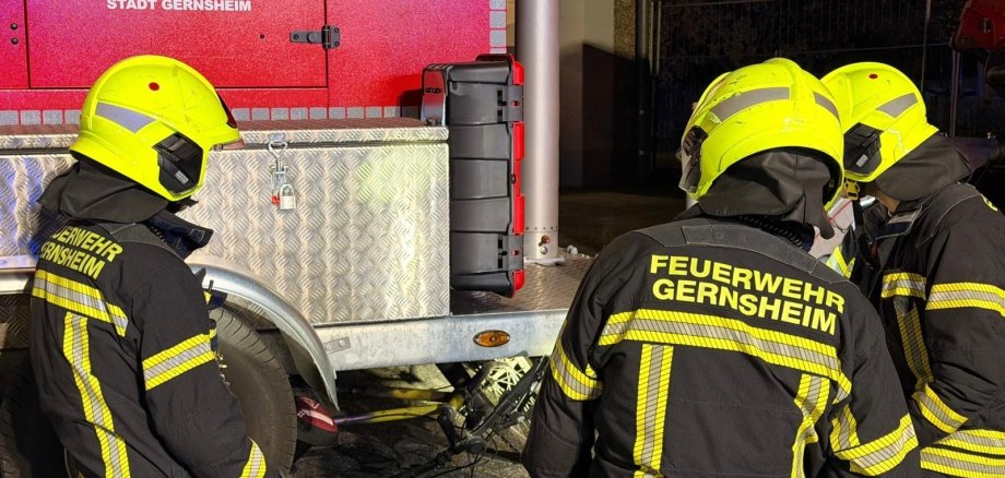 Drei Feuerwehrleute in Einsatzkleidung knien an einem Anhänger während einer technischen Rettungsübung. Unter dem Anhänger befindet sich ein Fahrrad.