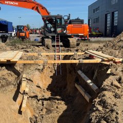 Feuerwehrleute in Schutzkleidung arbeiten gemeinsam an einer Übung im Bereich Technische Hilfeleistung am Bau mit einem Bagger.