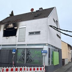 Wohnhaus. Die Fenster und das Dach sind nach einem Brand rußgeschwärzt. Vor dem Haus ist eine Absperrung aufgestellt.
