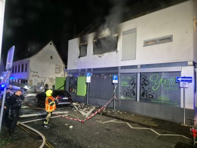 Ausgebranntes Wohnhaus bei Nacht. Im Vordergrund steht ein Feuerwehrmann und zwei Polizisten.