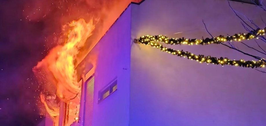 Flammen schlagen aus zwei Fenstern im 1. Stock eines Wohnhauses.