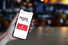Eine Hand hält ein Smartphone mit der geöffneten Warn-App NORA. Der Hintergrund ist verschwommen.
