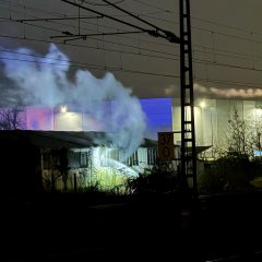 Weißer Rauch dringt aus der Lagerhalle - die Brandbekämpfung zeigt somit erste Erfolge.