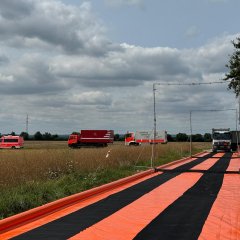 Eine aufgebaute Fahrzeugdekontaminationsschleuse. Im Hintergrund ein Acker und drei Feuerwehrfahrzeuge.