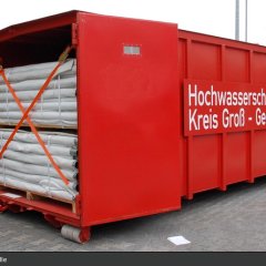 Roter Abrollbehälter der Feuerwehr für Hochwasserschutz (AB-HWS-1). Geöffnete Tür mit Blick auf Dammbaumaterial.