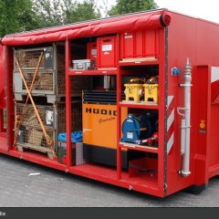 Roter Abrollbehälter der Feuerwehr für Hochwasserschutz (AB-HWS-2). Geöffnete Seite mit Blick auf eine Sandsackfüllmaschine.