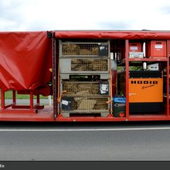 Roter Abrollbehälter der Feuerwehr für Hochwasserschutz (AB-HWS-2). Geöffnete Seite mit Blick auf eine Sandsackfüllmaschine.