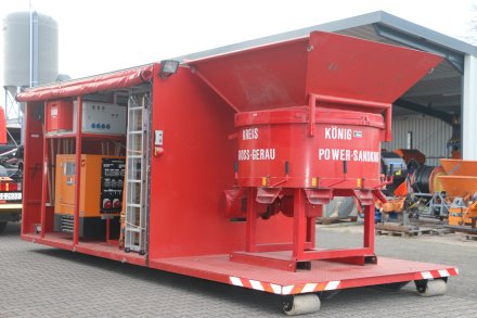 Roter Abrollbehälter der Feuerwehr für Hochwasserschutz (AB-HWS-2). Geöffnete Seite mit Blick auf eine Sandsackfüllmaschine.