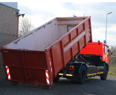 Roter Abrollbehälter Mulde der Feuerwehr  (AB-M) wird von einem Feuerwehrfahrzeug abgekippt.