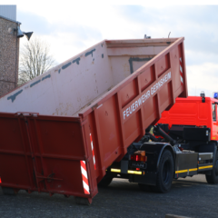Roter Abrollbehälter Mulde der Feuerwehr  (AB-M) wird von einem Feuerwehrfahrzeug abgekippt.