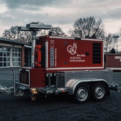 Roter Notstromanhänger vor einem Feuerwehrgerätehaus.