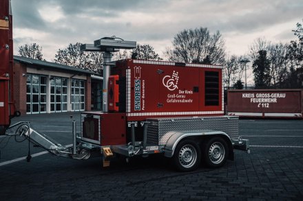 Roter Notstromanhänger vor einem Feuerwehrgerätehaus.