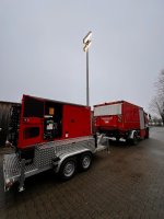 Roter Notstromanhänger mit Lichtmast an einem Feuerwehrfahrzeug.