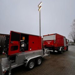 Roter Notstromanhänger mit Lichtmast an einem Feuerwehrfahrzeug.