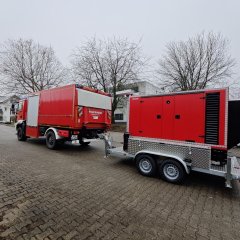 Roter Notstromanhänger mit Lichtmast an einem Feuerwehrfahrzeug.