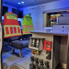 Innenraum eines Feuerwehr-Einsatzfahrzeugs mit Sitzen, Warnwesten für Zugführer und Einsatzleiter sowie Funk- und Arbeitstechnik.
